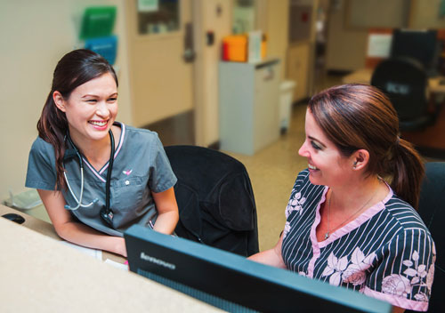 Picture of a female Physician and male Nurse walking down a hospital hallway talking.