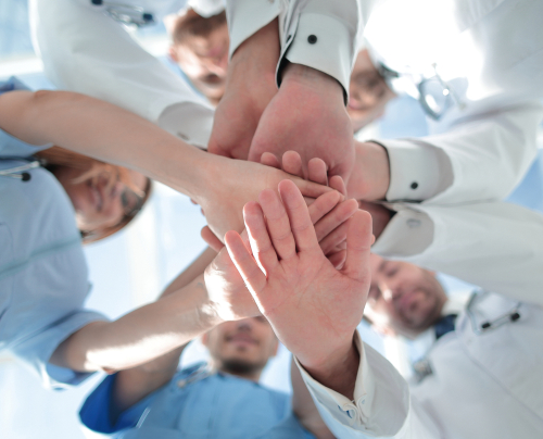 Picture of five smiling medical professionals standing in a circle with all of their hands placed on another.