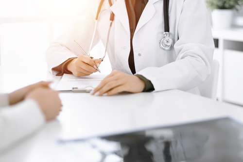 Female Physician is sitting down at a table writing on patient paperwork report.