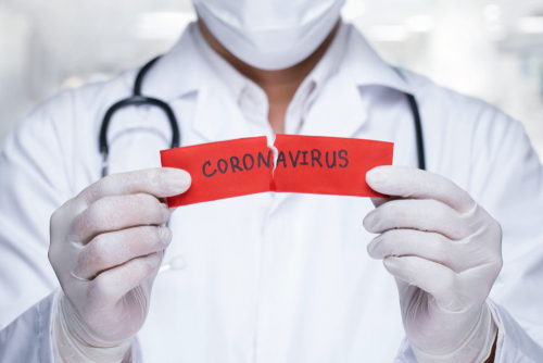 Picture of a male Physician wearing gloves and holding a ripped piece of paper that says Coronavirus.
